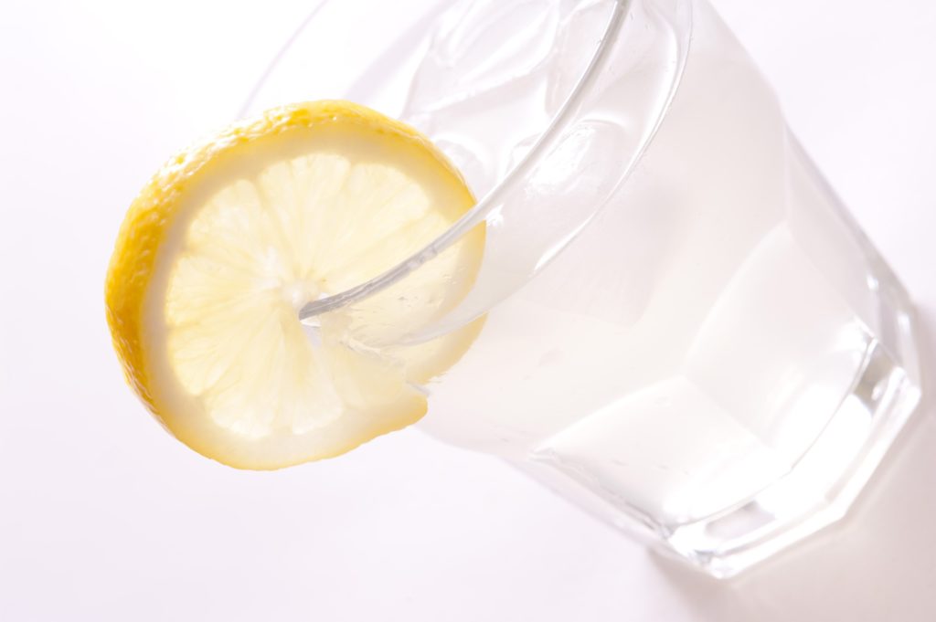 Angled view of a cold glass of gin and tonic garnished with a slice of fresh lemon served with ice